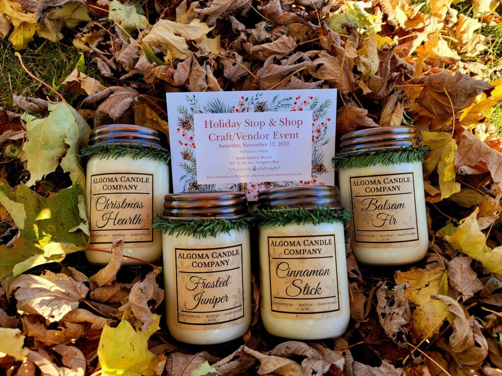 four Algoma Candle Company holiday candles in a pile of leaves